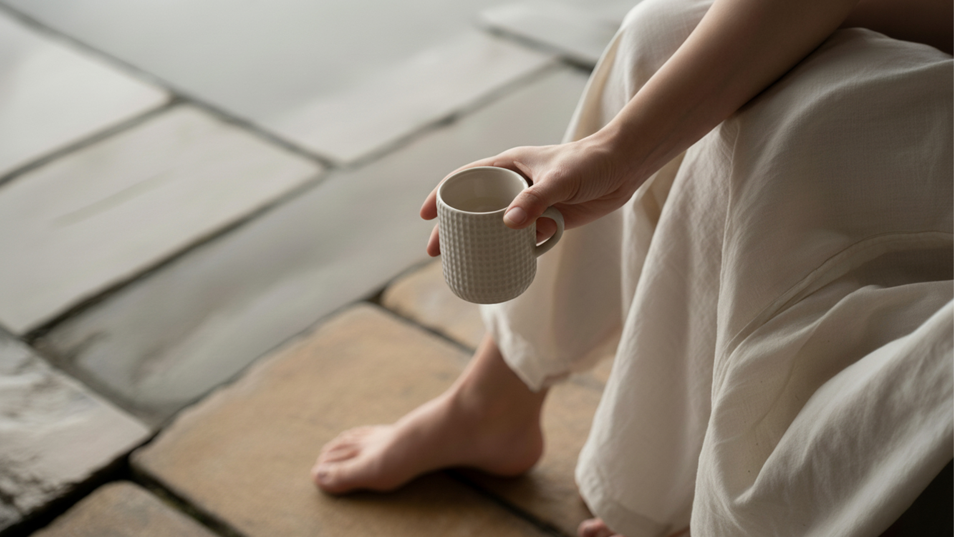 Close-up of a person in linen clothing holding a textured ceramic mug, creating a sense of calm.